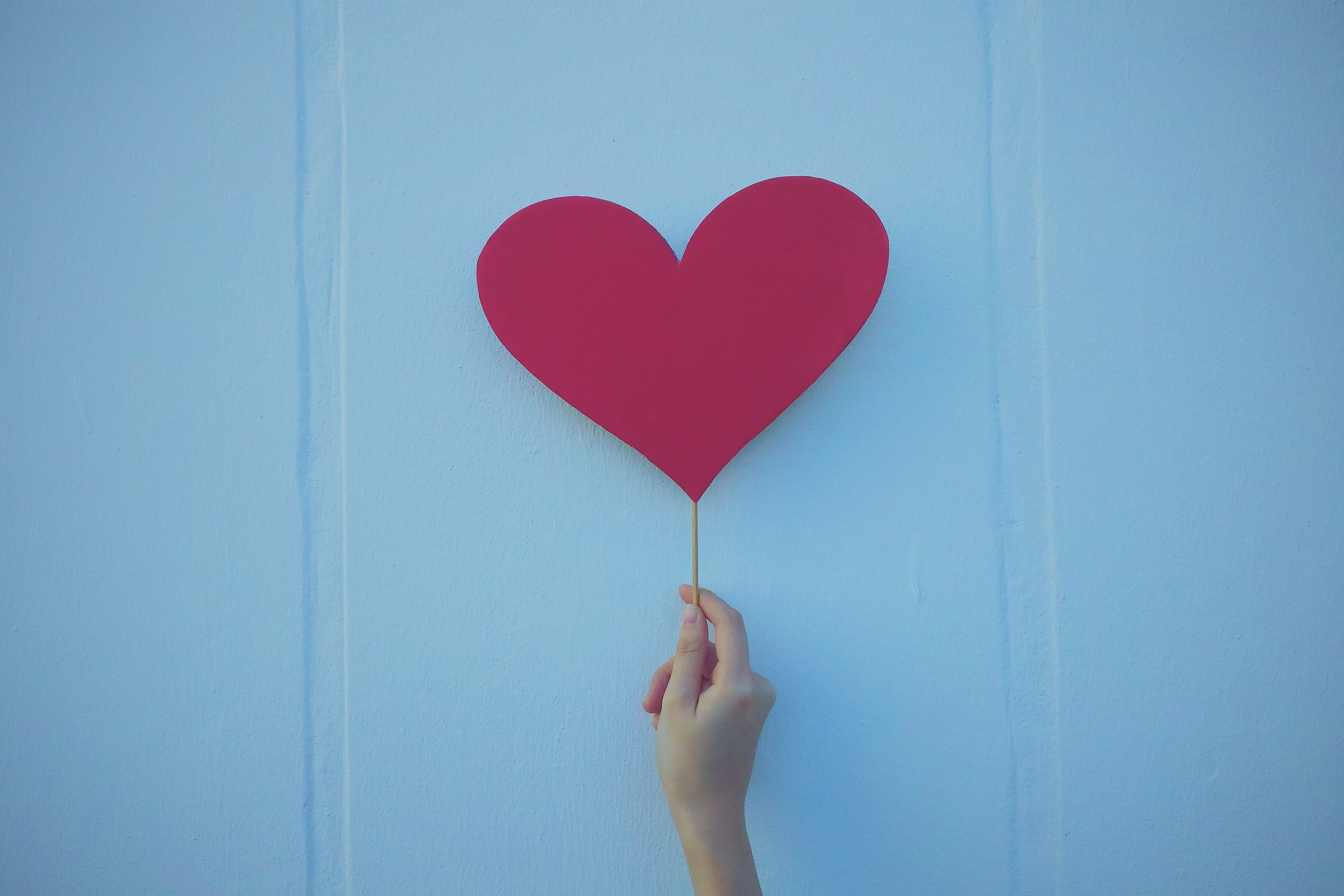 An image of a hand holding up a paper heart on a stick in front of a blue background